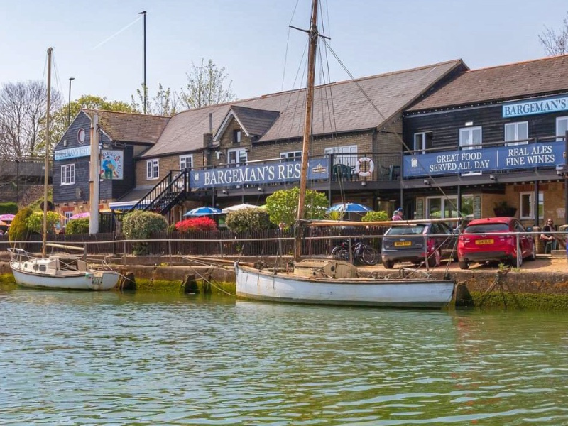 A pub on the riverside, with the river in the foreground and boats against the railings