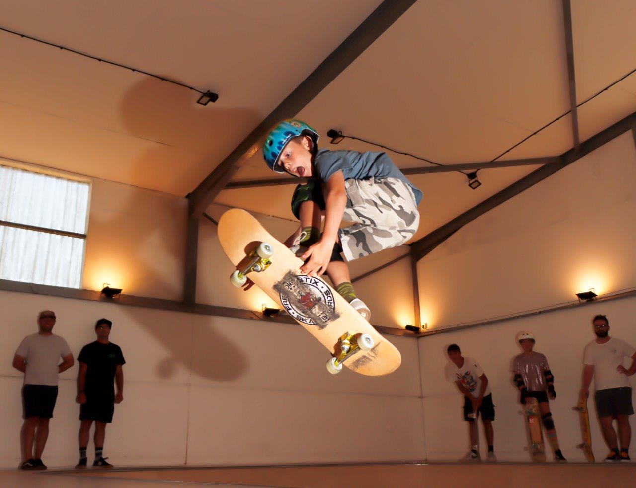 A white male skateboarder is in the air at an indoor skate facility on the Isle of Wight