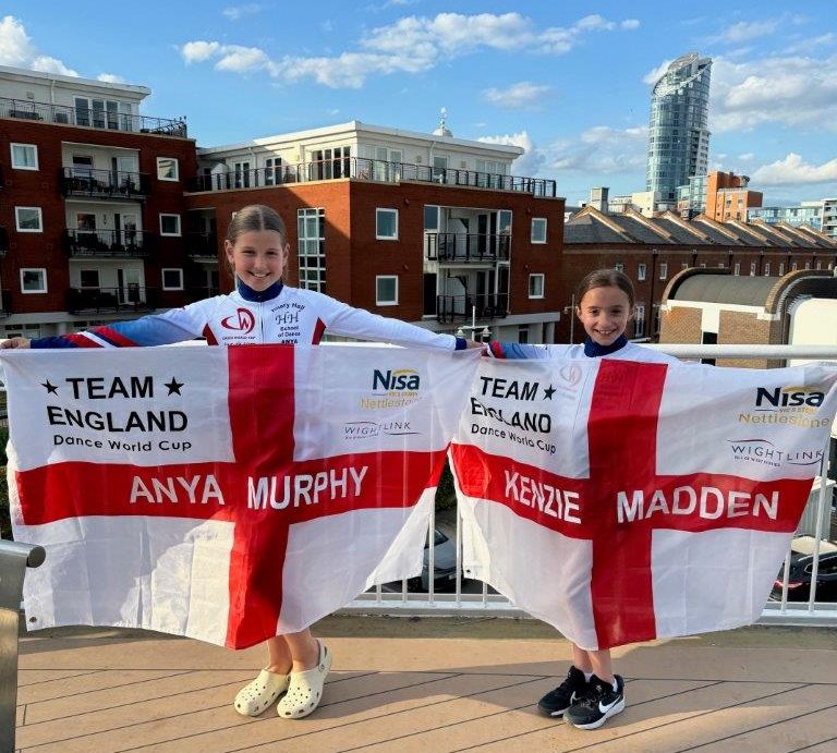 Two girls holding Team England flags onboard a ferry with Portsmouth in the background