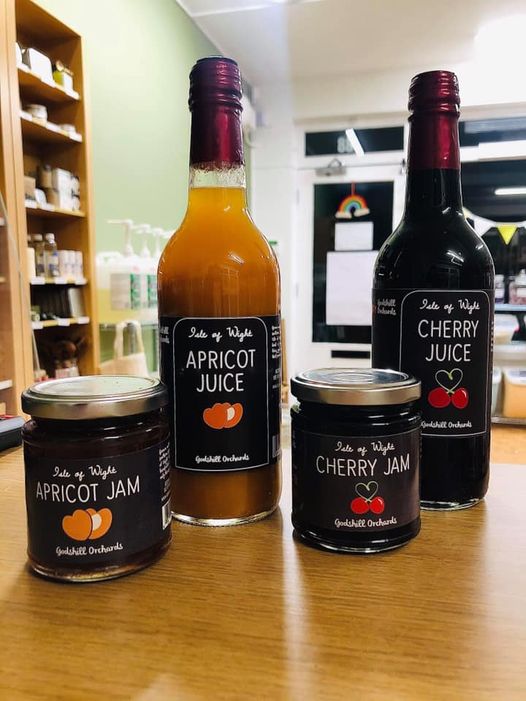 A bottle of apricot juice and apricot jam alongside a jar of cherry jam and bottle of cherry juice, with the backdrop of a food store