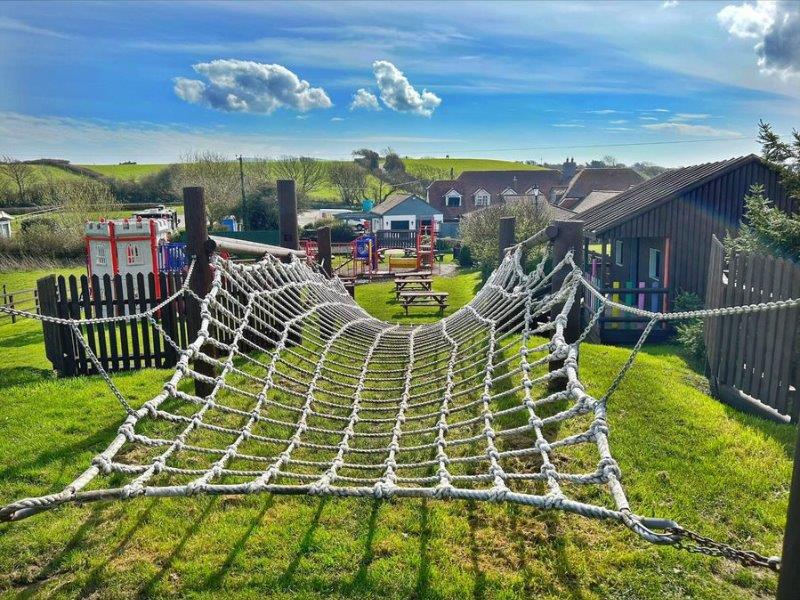 A children's climbing net in a pub garden, with other play equipment in the background. The pub is in the countryside