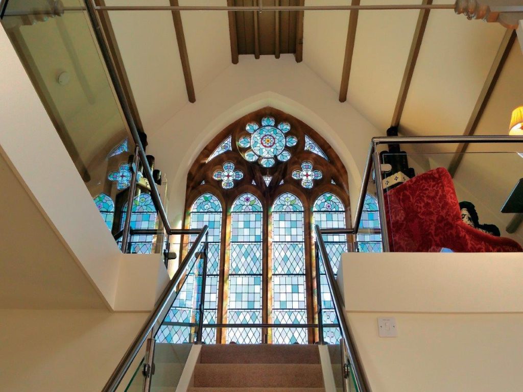 Inside a former church which has been converted to visitor accommodation. You can see up the stairs towards an impressive stained glass arch window.