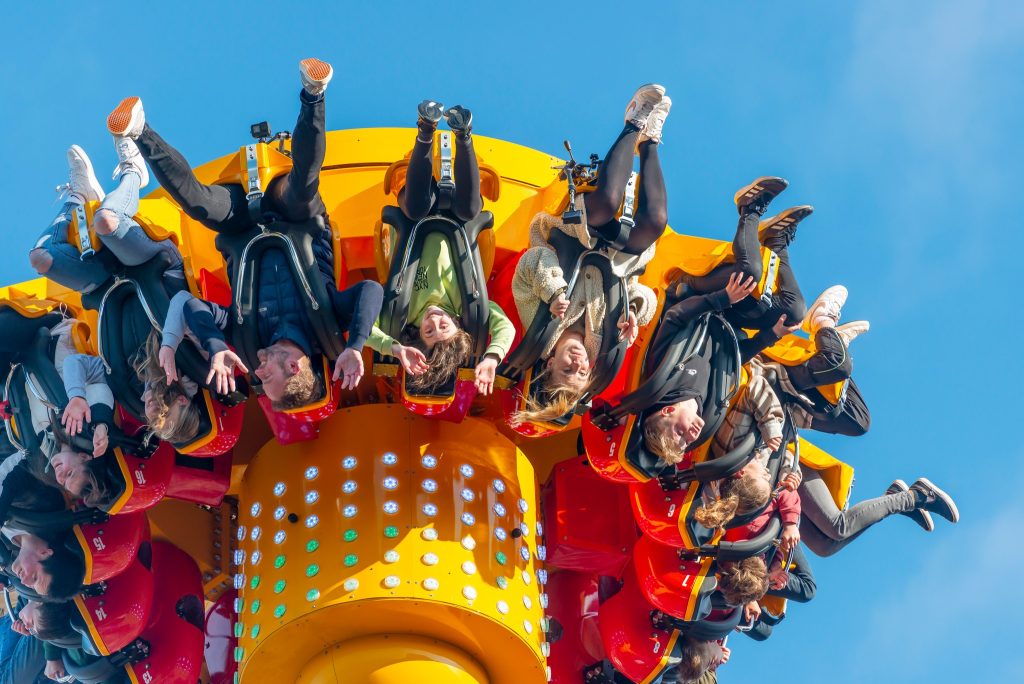 A fairground ride which shows riders upside down. The ride is brightly coloured in red and yellow, against a clear blue sky.