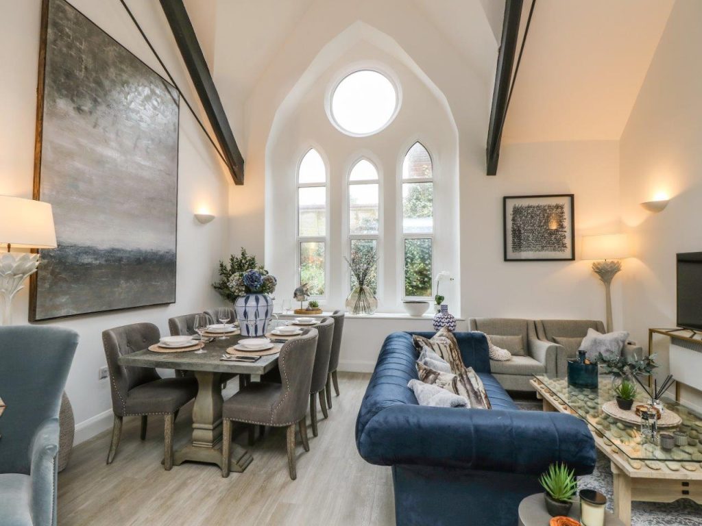 Inside a church that's been converted into visitor accommodation, it's light and airy with a arched window. There's a sofa and dining table in this lounge area.