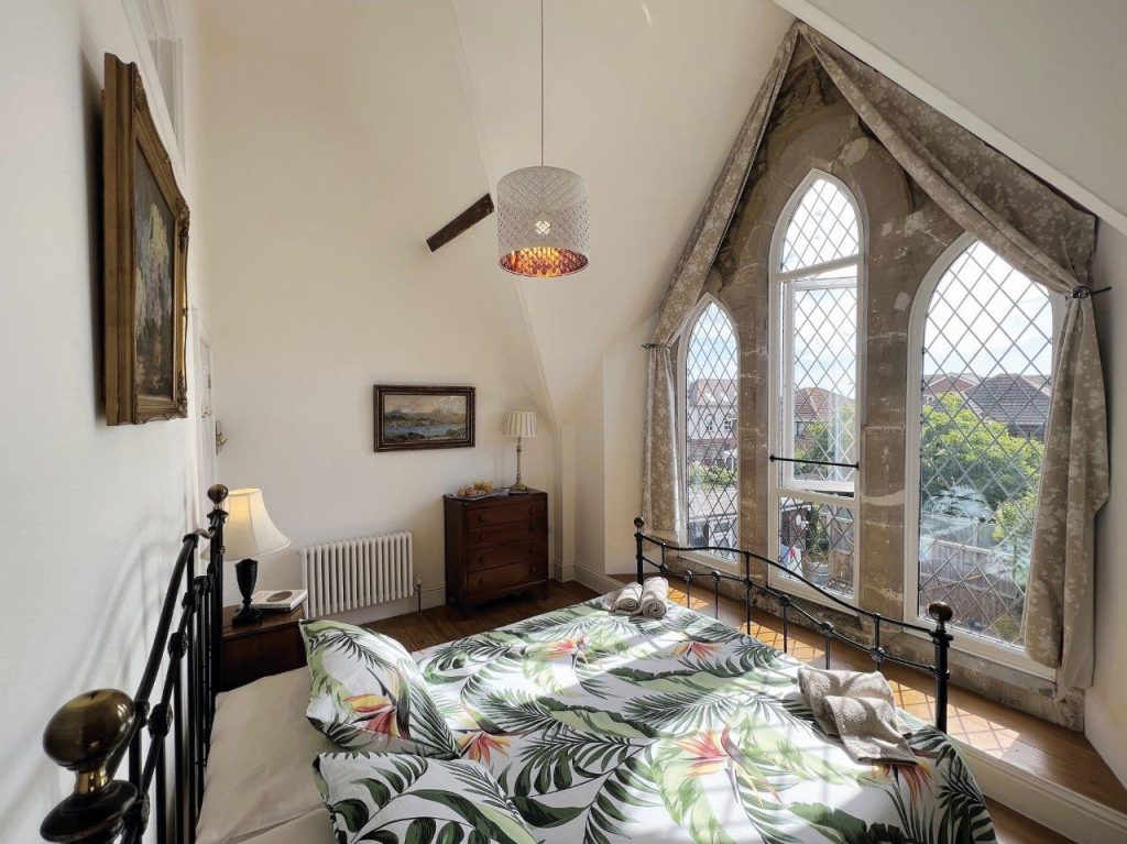 Inside an old Wesleyan church which has been converted to visitor accommodation. We can see a double bedroom with impressive arched windows