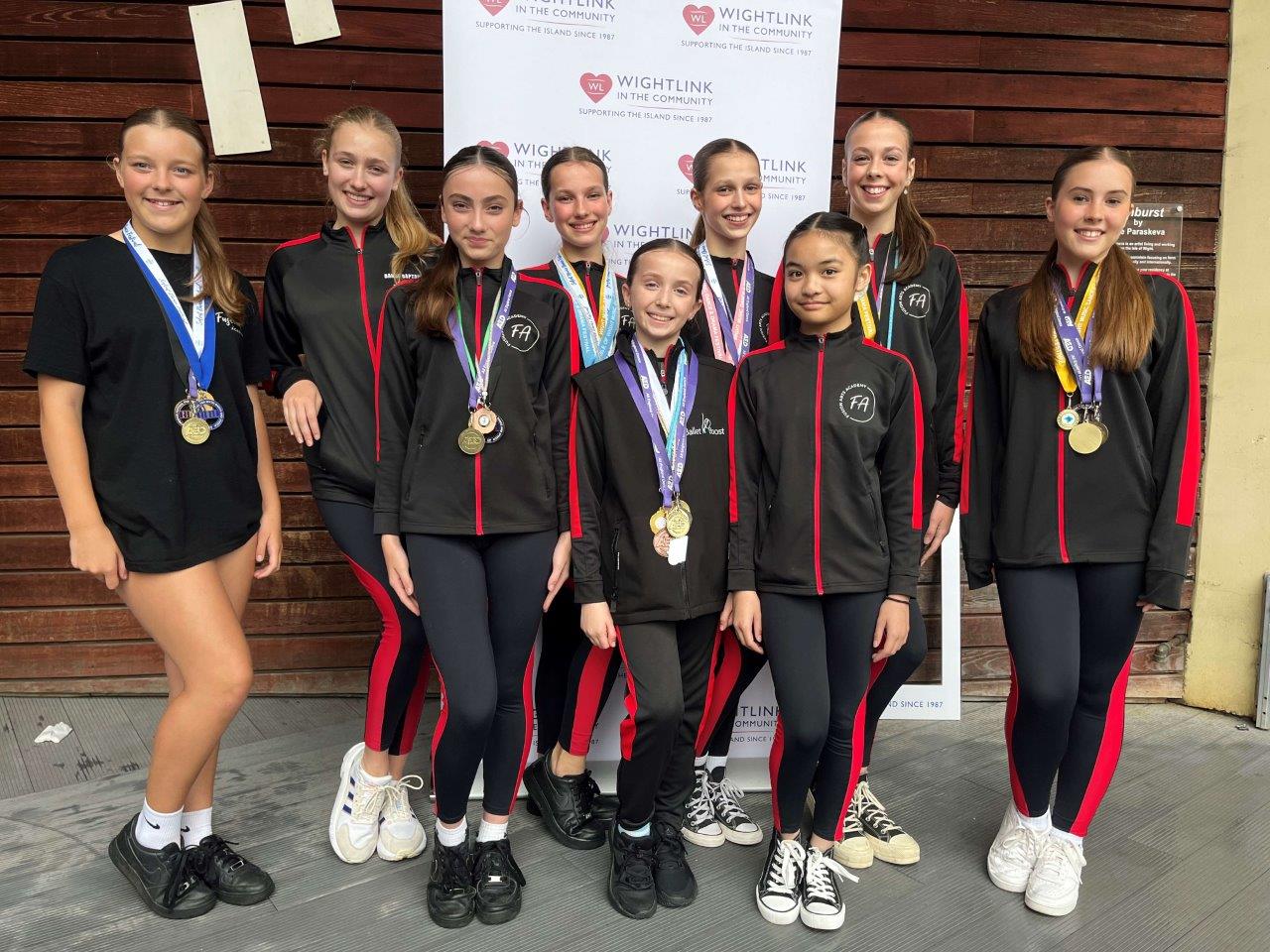 A group of girls in matching sports outfits, wearing medals, against a backdrop that says 'Wightlink in the Community'