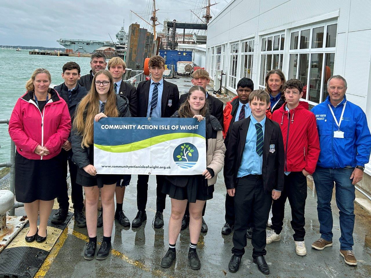 A group of school children on the edge of a dock, in front of HM Naval Base Portsmouth