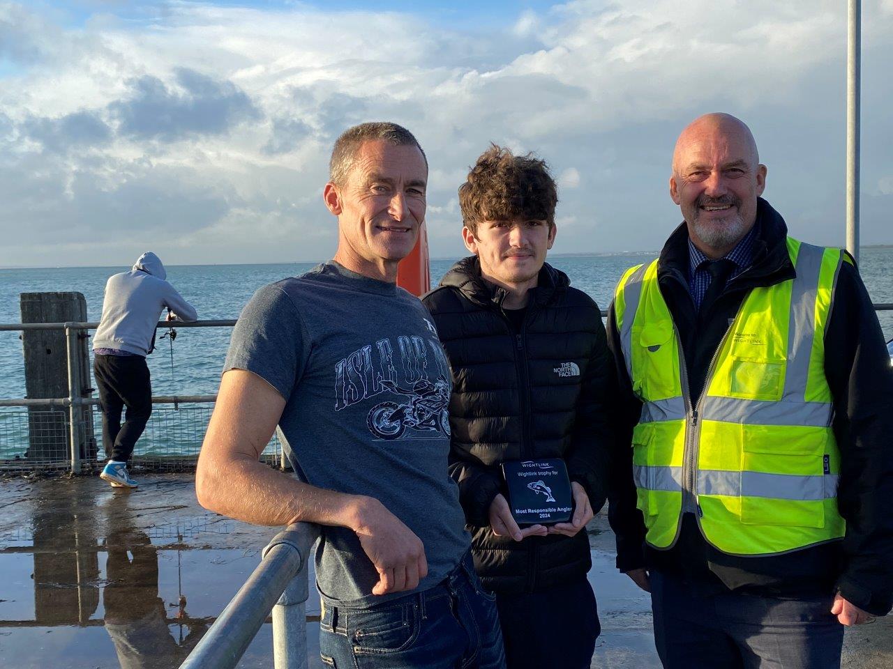 Three men standing near the edge of a pier, one of them is holding a trophy