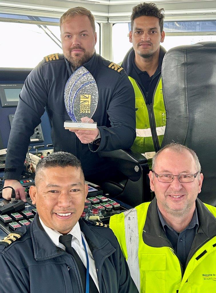 Four man inside the bridge of a catamaran ship holding a trophy