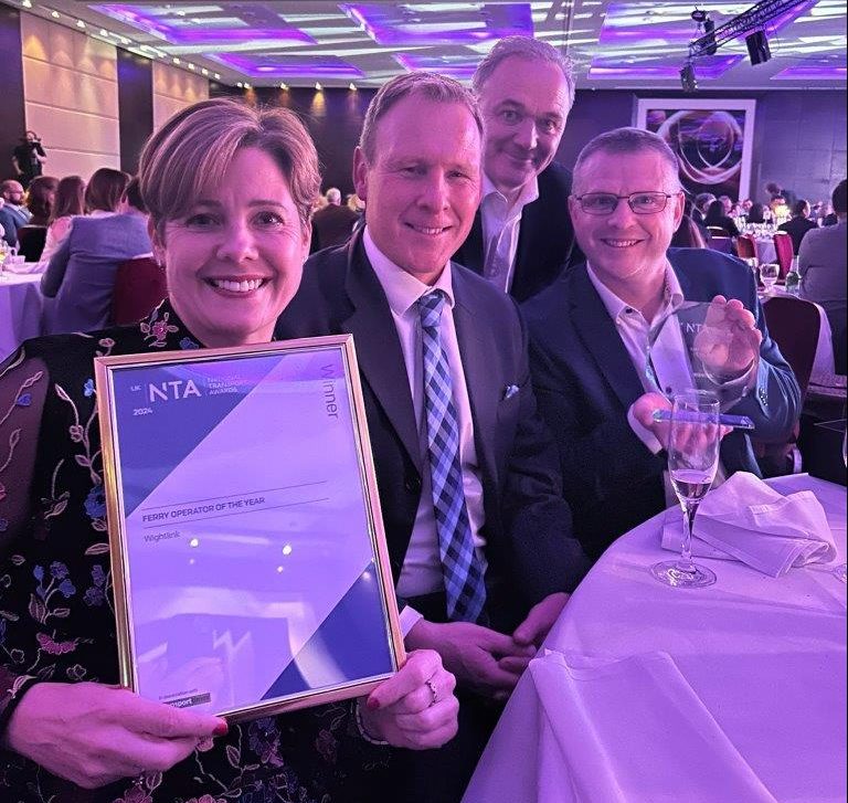 Four people in a meeting room in London smiling and holding an award framed in a picture frame