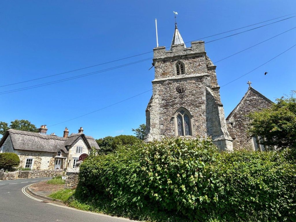 A traditional English village scene with a church tower and thatched houses