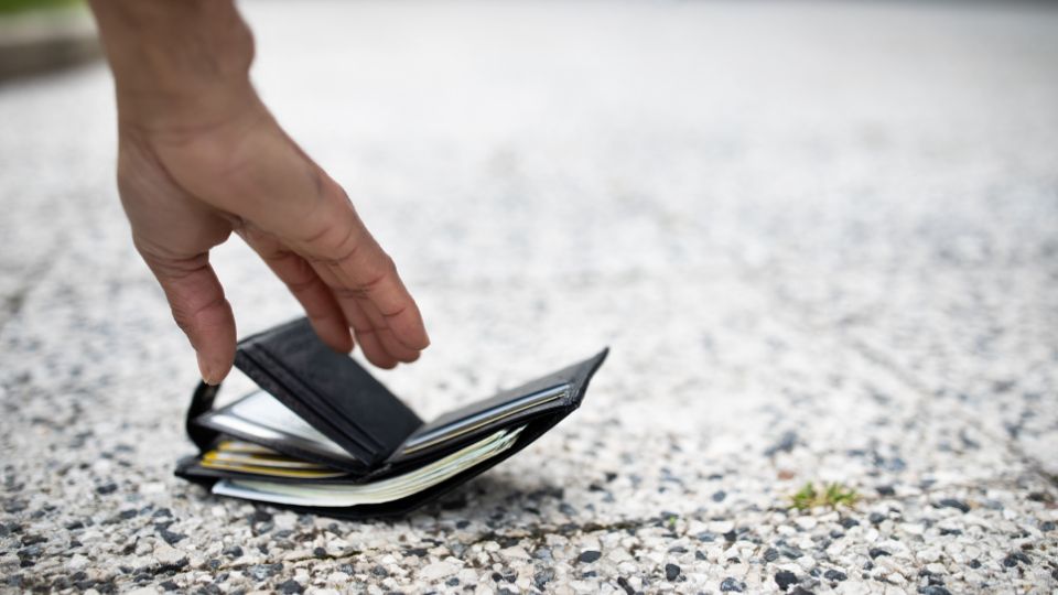 A close up image of a hand picking up a wallet from the ground