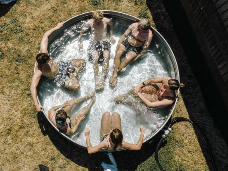 Looking down on a large ice bath with 6 people in it, the bath is on grass.