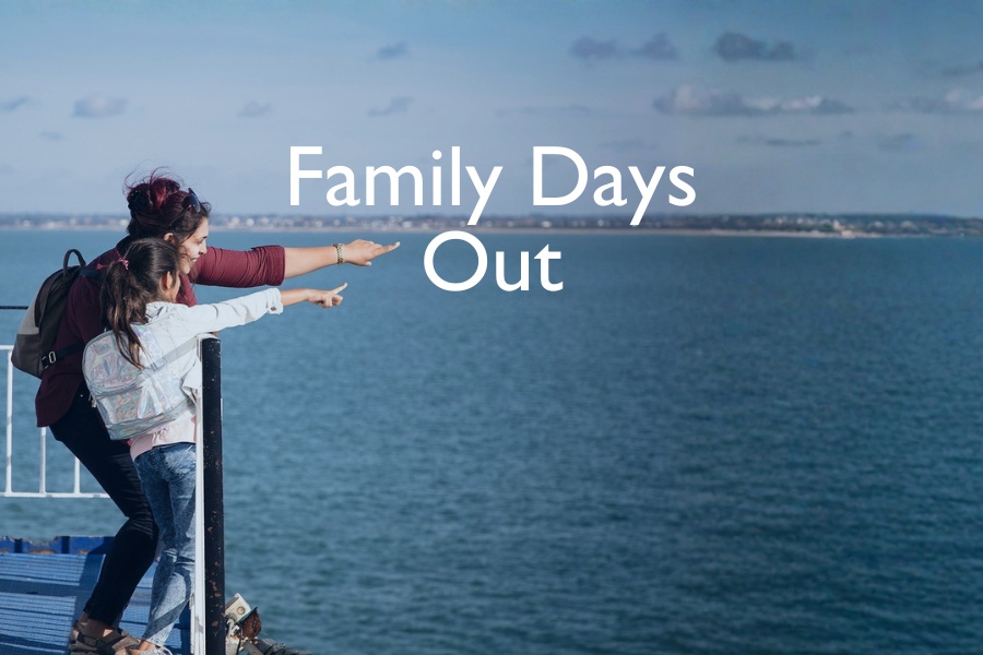 A mother and daughter stand on the deck of a Wightlink ferry, smiling and pointing towards the distant coastline, with the words “Family Days Out” overlaid on the image.