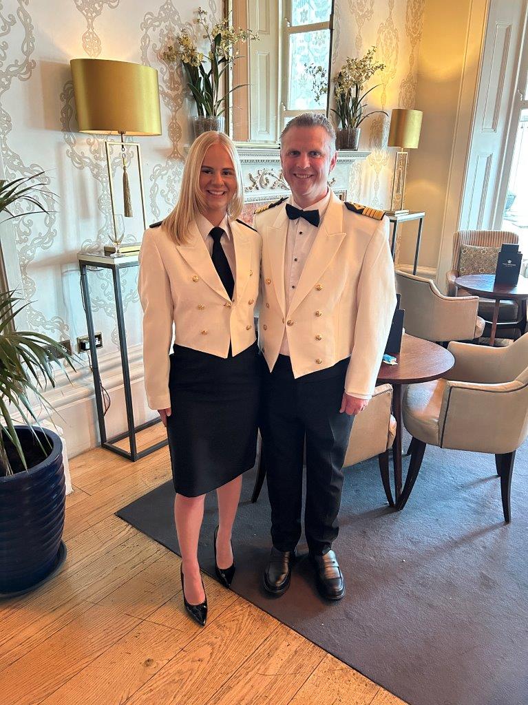 A man and a woman, wearing dress uniform, pose for a photo in a hotel lobby