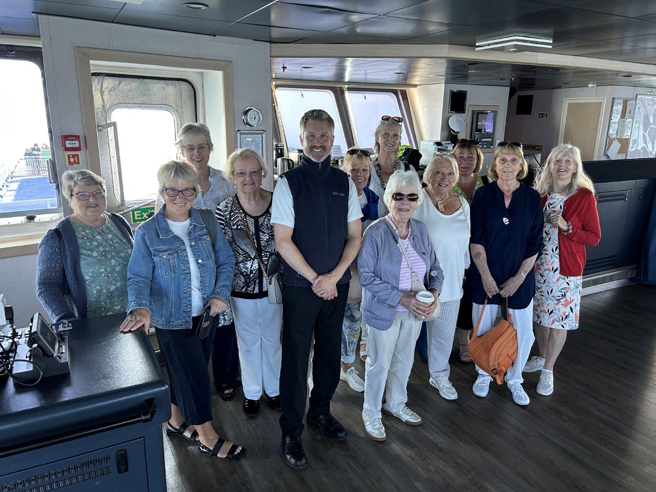 A group of women stand with a ferry captain on the Bridge of a ferry