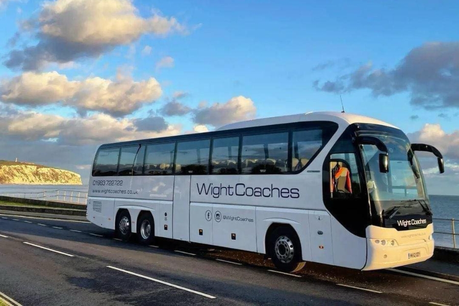 Coach with branding 'Wight Coaches' on side, in front of a seaside view with wight cliff and blue skies behind.