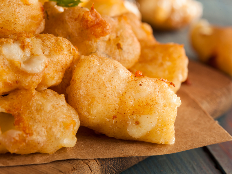A plate of small items battered in golden batter, on top of greaseproof paper and a wooden board