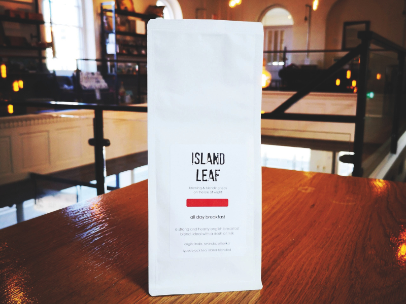 A white packet of tea, called 'Island Leaf' is on a table in a coffee shop