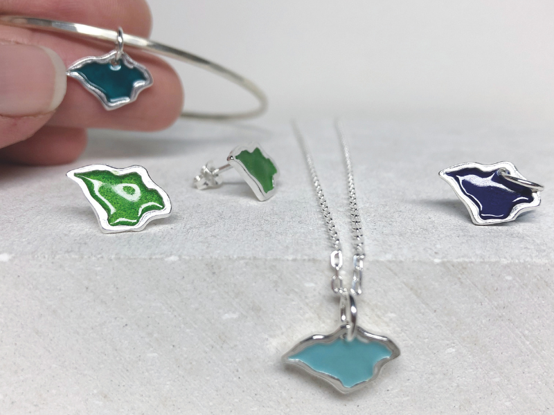 Small jewellery pendants in the shape of the Isle of Wight. Made from silver and coloured enamel, some are on necklaces, others on bracelets and earrings.
