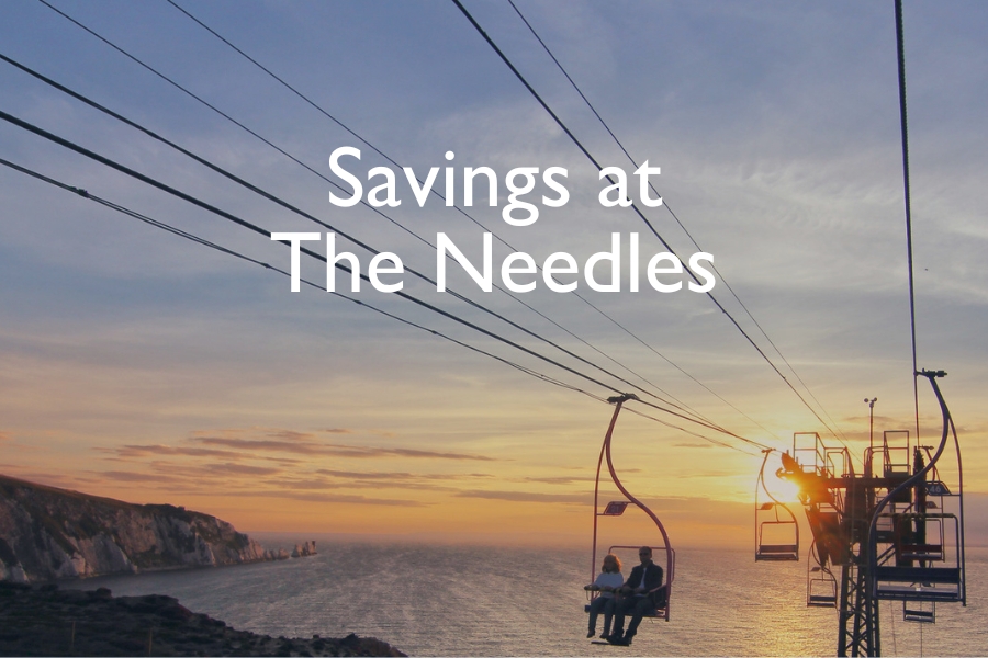 People ride the chairlift at The Needles on the Isle of Wight during sunset, with the cliffs and sea in the background and the text “Savings at The Needles” overlaid on the image.