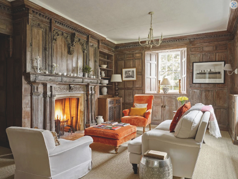 An opulent wood-paneled lounge with sofas, foot stool, fireplace and wall paintings