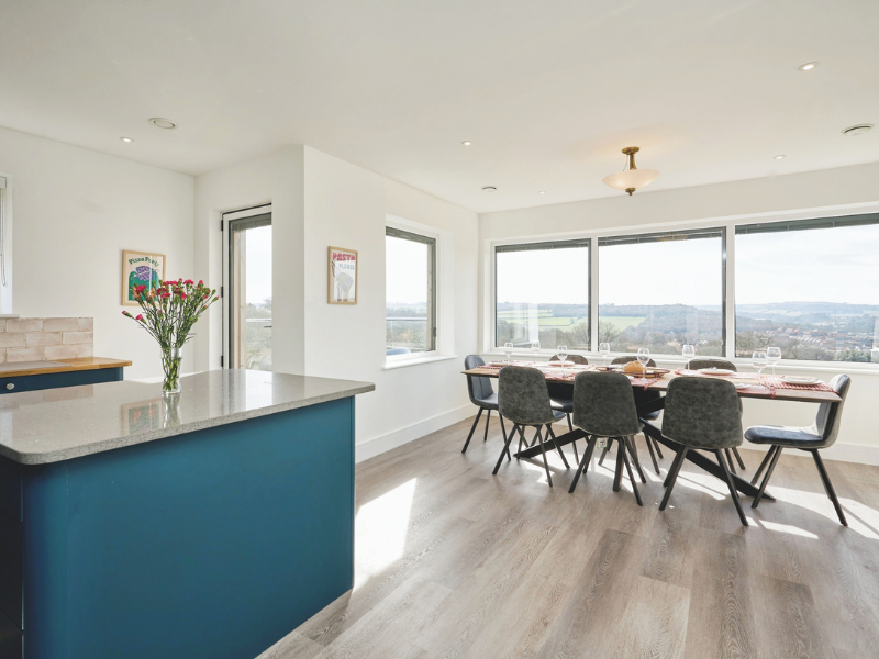 A modern kitchen and dining room with panoramic windows, clean lines, white and teal colouring