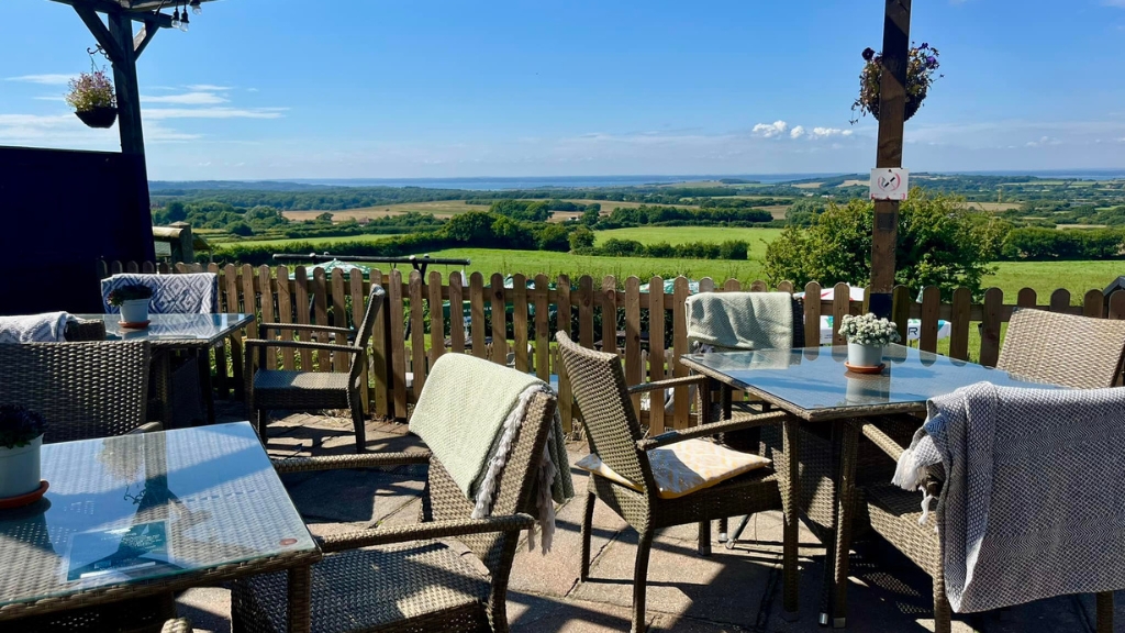 Outdoor dining area with wicker chairs and glass tables looking out over rolling green countryside and farmland on the Isle of Wight