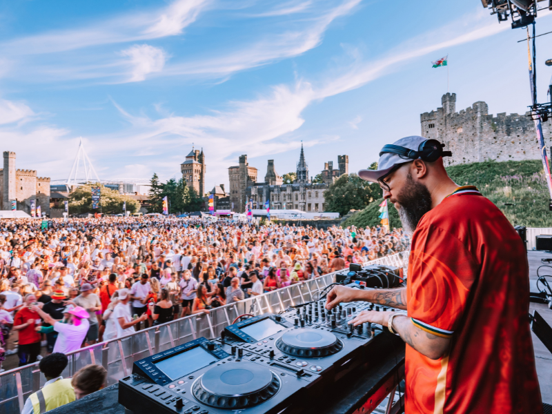 A DJ using music decks on a stage overlooking a crowd in the grounds of a castle - thanks to VisitBritain/Sin Lam/Depot Cardiff