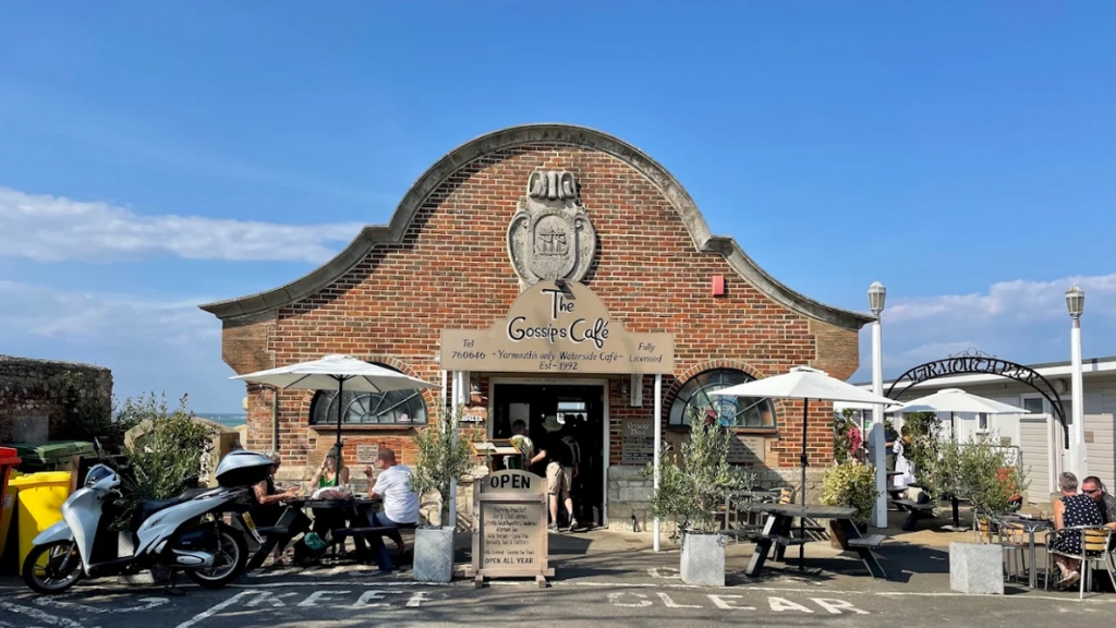 Front entrance of Gossips Café in Yarmouth with outdoor seating, umbrellas and people dining beside the waterfront.