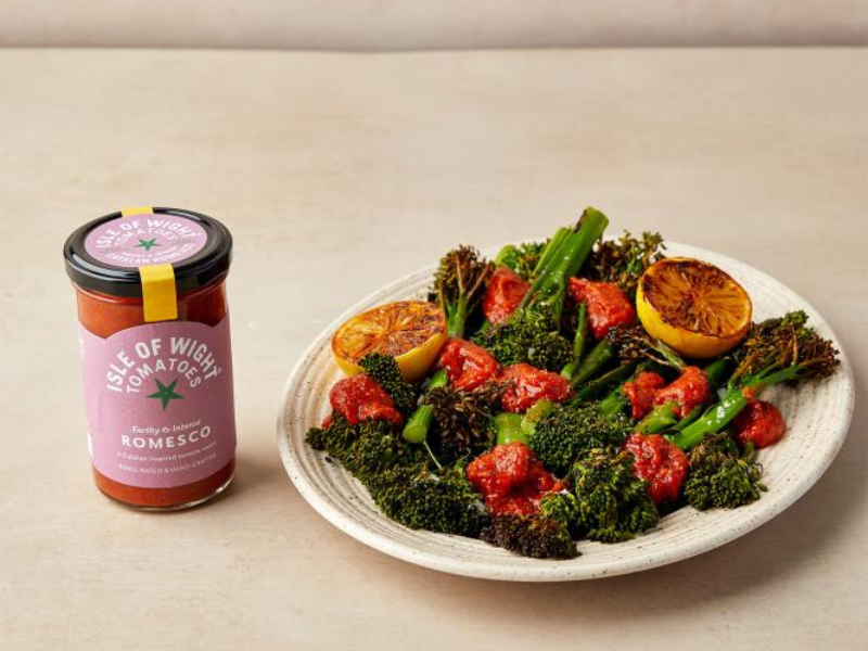 A plate of vegetables on a beige table and backdrop. There's a bottle of sauce nearby