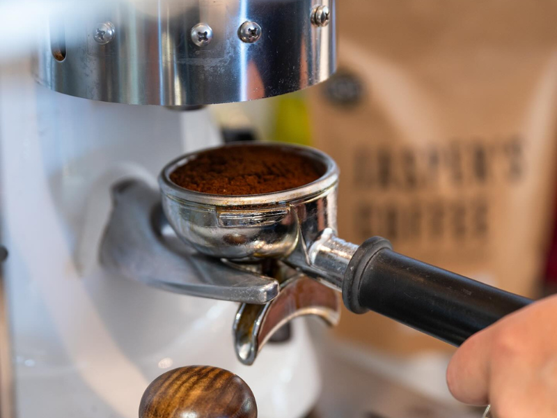 An espresso machine with someone operating it, putting the coffee in the machine