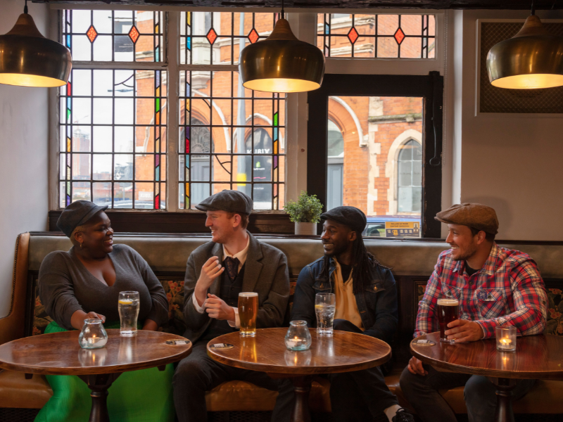 A group of friends in a traditional pub wearing peaked caps - credit; VisitBritain/Rod Edwards