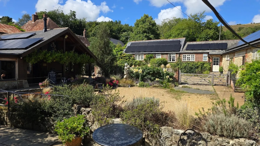 Charming rural courtyard with plants, solar-topped farm buildings and outdoor dining area at The Garlic Farm on the Isle of Wight.