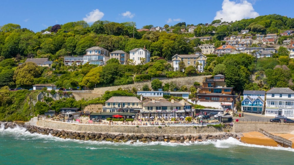 Ventnor seafront lined with restaurants and houses on the hillside above, with waves breaking along the coastal wall.