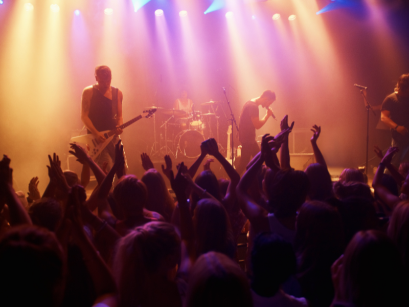 A live music venue, taken from in the crowd, with a band on stage playing guitars and singing