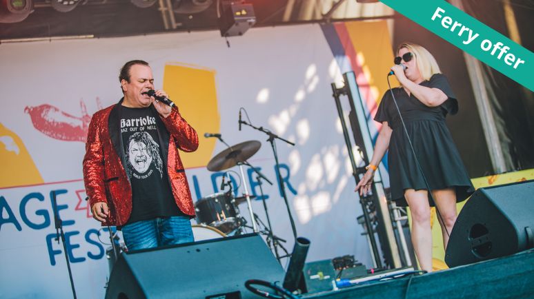Two singers perform live on an outdoor stage during a festival, with microphones and instruments visible. A ribbon in the corner reads “Ferry offer”.