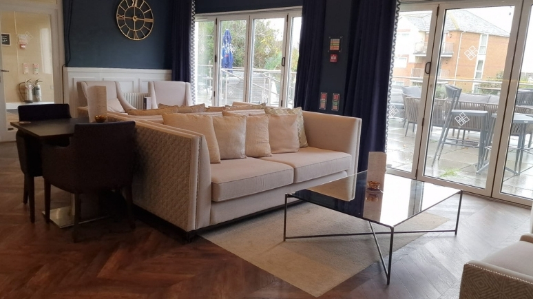 A comfortable lounge area with sofas and a glass coffee table, opening onto an outdoor terrace through large glass doors.