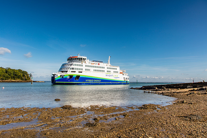 Wightlink’s hybrid ferry Victoria of Wight sailing in calm waters near the Fishbourne shoreline under a clear blue sky.