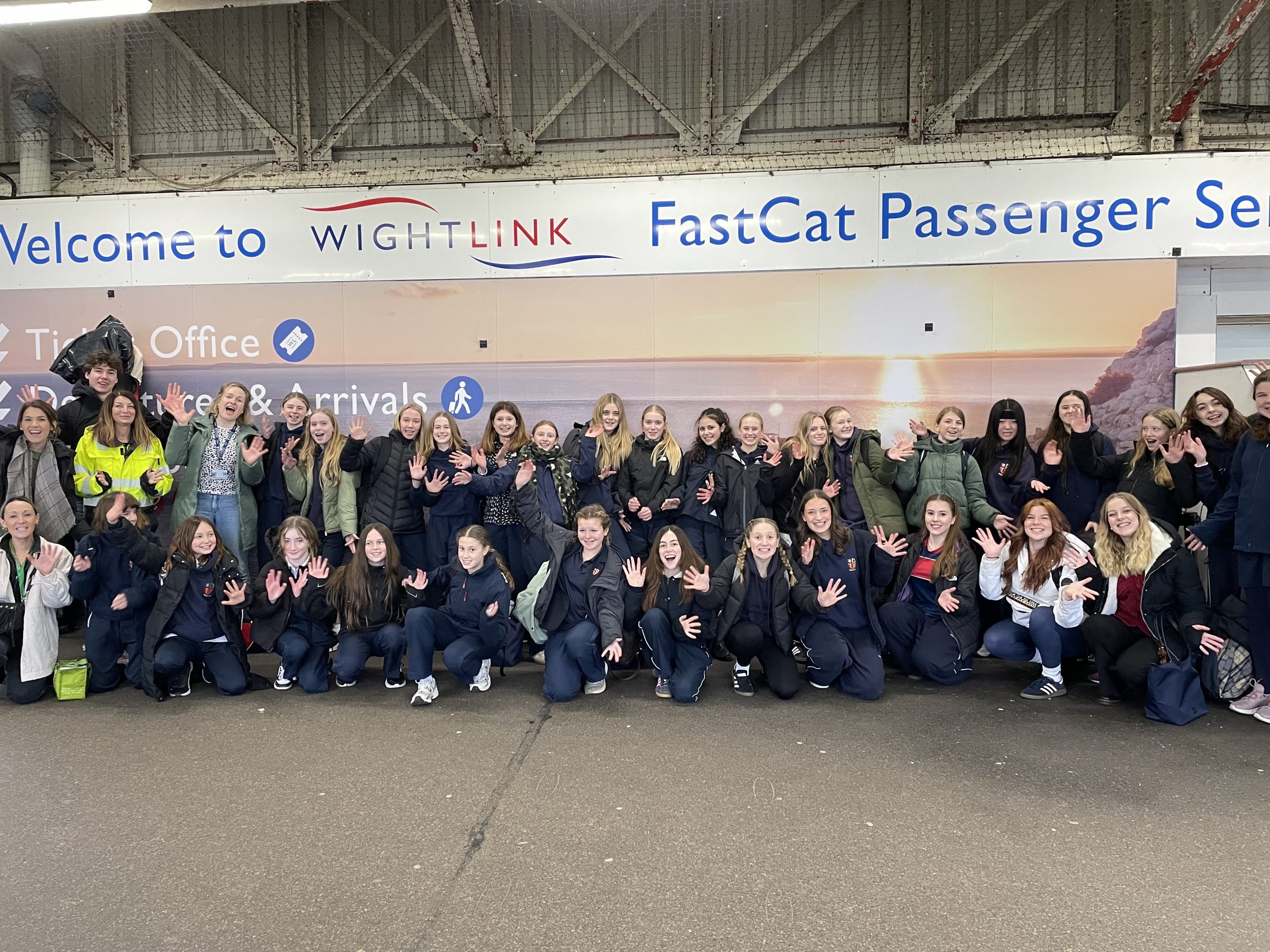 Large group of schoolchildren and teachers waving and smiling inside Wightlink’s FastCat passenger terminal in Ryde, standing beneath a “Welcome to Wightlink” sign.