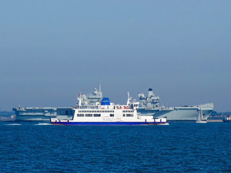 A Wightlink ferry on the Solent is next to a grey Royal Navy vessel