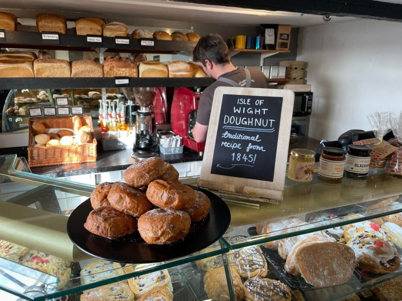 A plate of doughnuts on the counter of a bakery with a chalk board sign next to it