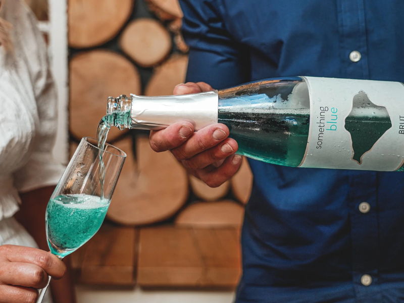 A person in a blue shirt pours a flute of Adgestone blue sparkling wine from a bottle.