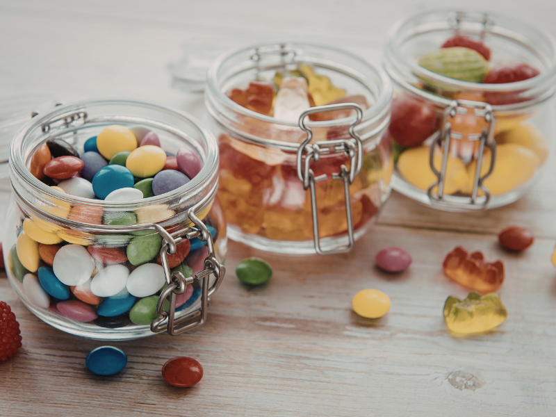 A trio of kilner jars filled with sweets, with some spilling out onto the table