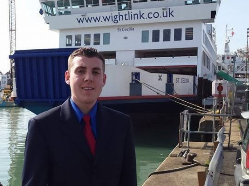 A young man wearing a suit in front of Wightlink's St Cecilia ferry in dock