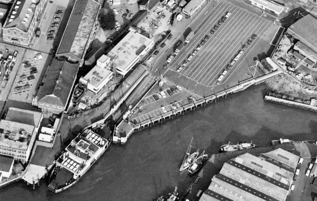 Aerial black and white view of the Gunwharf terminal in Portsmouth, showing ferry berths, parked cars and surrounding dockyard buildings.