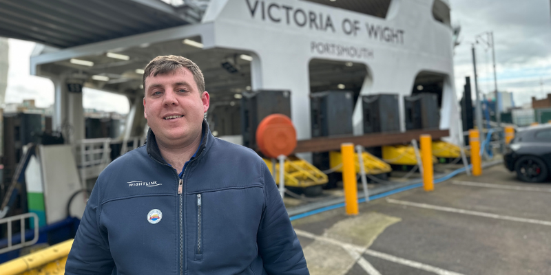A man with a Wightlink branded fleece stands against a Wightlink ferry - Victoria of Wight