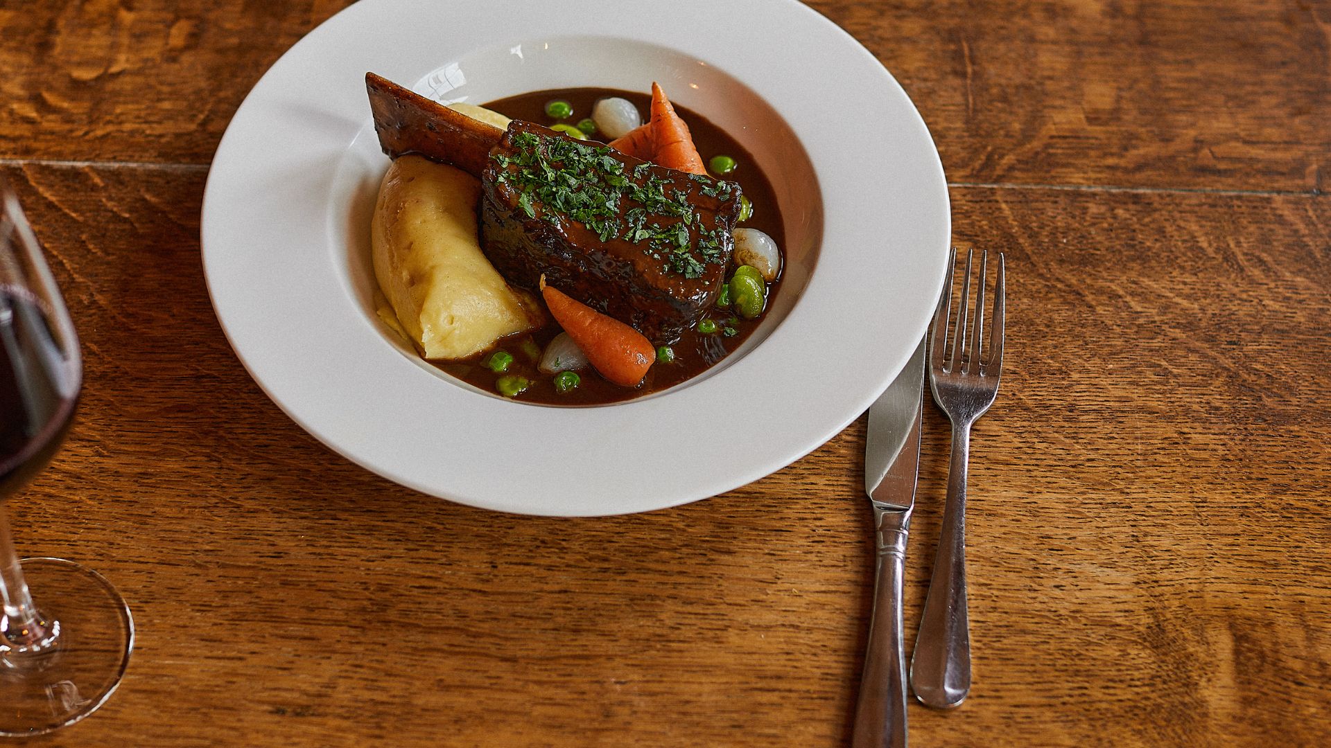 Plated main course at Brasserie Blanc featuring braised meat, vegetables and mashed potato on a wooden table.