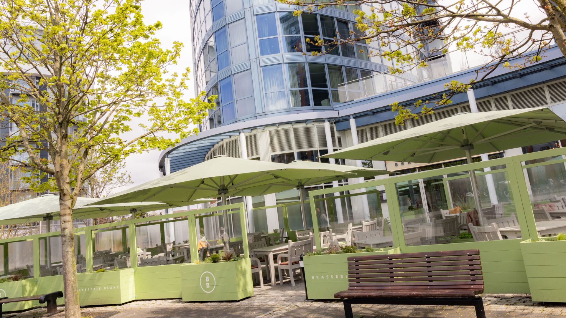 Outdoor seating area at Brasserie Blanc Portsmouth with green parasols, tables and a modern building backdrop.