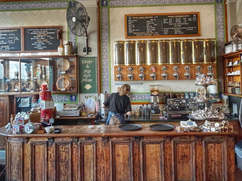 Inside a chocolate shop, looking at the counter which is wood panelled and has various hot chocolate dispensers avove it